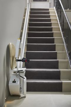 Zusammengeklappter gerader Treppenlift neben einer Treppe mit Teppichbelag