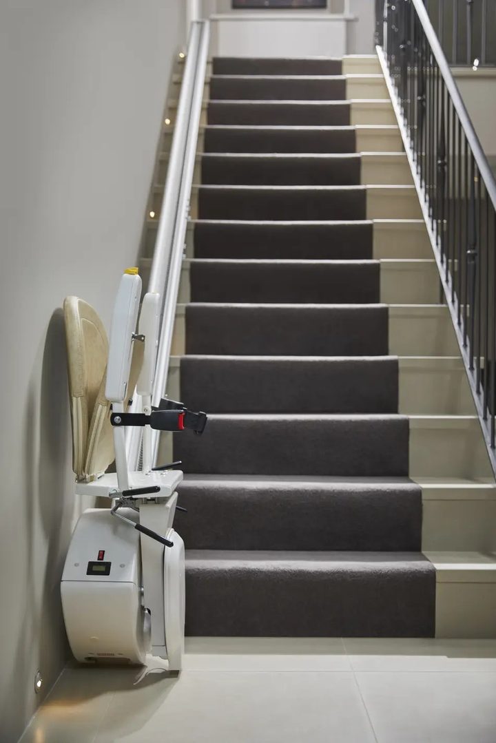 Zusammengeklappter gerader Treppenlift neben einer Treppe mit Teppichbelag