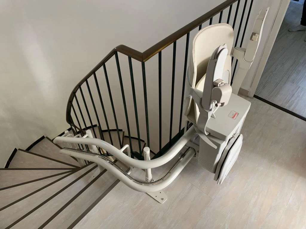 Zusammengeklappter Kurventreppenlift mit hochgeklapptem Sitz und Fußstütze am oberen Treppenabsatz